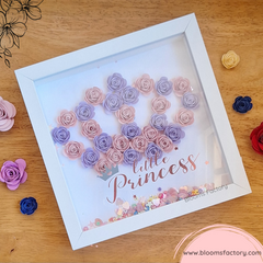 ¡Transforma la habitación de tu pequeña con nuestro Bloom Box “Little Princess” o "Pequeña princesa"! Este encantador cuadro está adornado con flores de papel hechas a mano, dispuestas en una corona y enmarcadas en un elegante marco blanco. Las flores en tonos pastel crean una pieza central visualmente atractiva que captura la esencia de la dulzura y la inocencia. Perfecto para añadir un toque de encanto y elegancia a cualquier espacio infantil o área de juego.