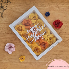 ¡Descubre la belleza en los detalles con este encantador cuadro decorativo! ‘Enjoy the Little Things’ está bellamente escrito entre flores de papel hechas a mano en tonos amarillos y naranjas creando una pieza que no solo es visualmente atractiva sino también inspiradora. Perfecto para añadir un toque de color y positividad a cualquier espacio. ¡Encuentra la alegría en los pequeños momentos! 