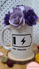 Taza decorativa coronada con flores de papel y un diseño de una batería descargada y el mensaje "Mom charging"