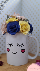 Taza decorativa coronada con flores de papel, la base está decorada con un rostro adorable de ojos tiernos y mejillas sonrosadas que te hará sonreír cada vez que la veas. 